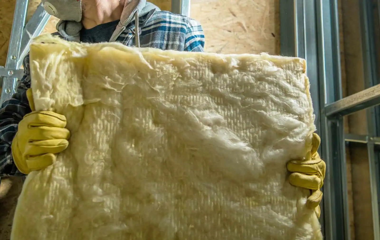 Worker installing fiberglass insulation in a building.