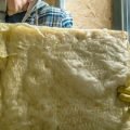 Worker installing fiberglass insulation in a building.